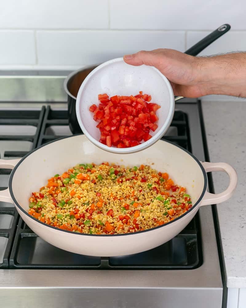 Adding chopped tomatoes to a pan to make fregola