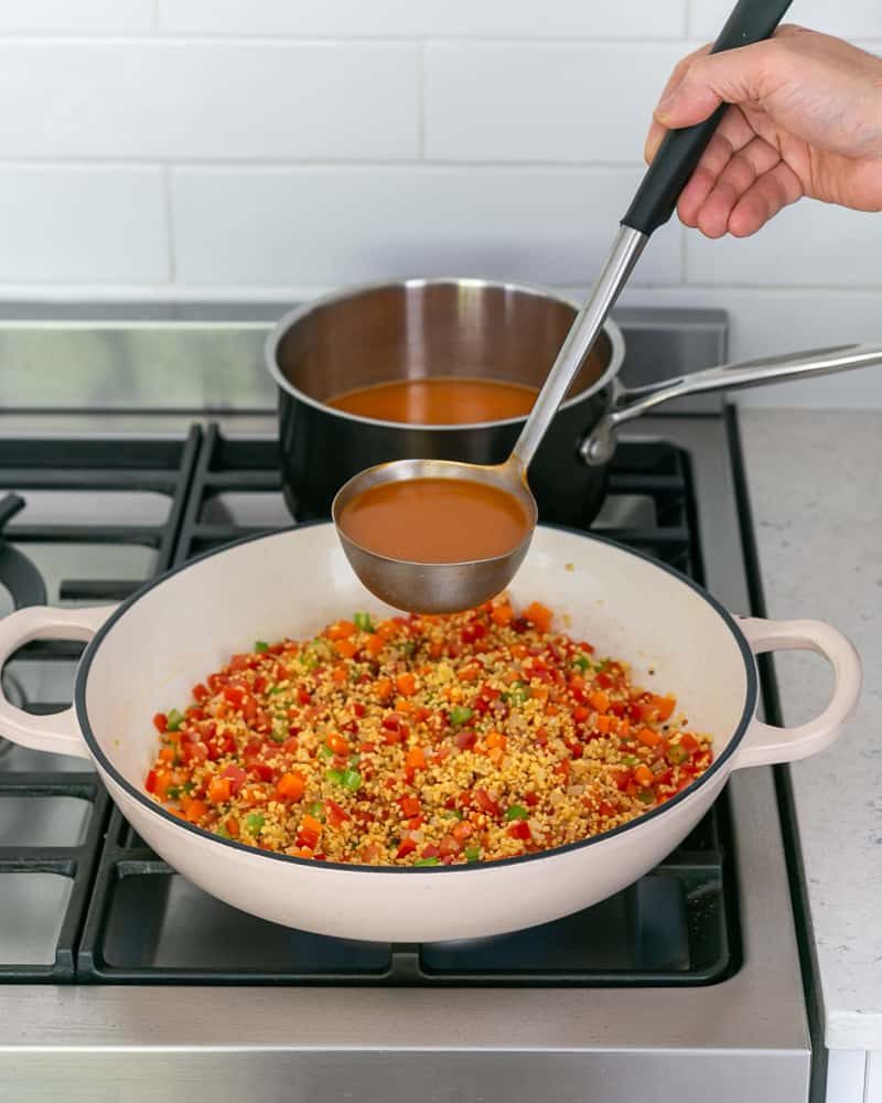 Adding prawn stock to cook fregola sarda and vegetables in the pan