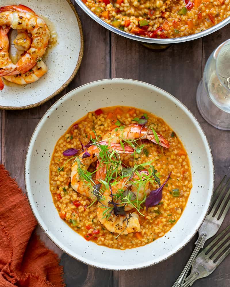 Garlic roasted prawns with fregola sarda individually plated in a bowl garnished with prawns and herbs