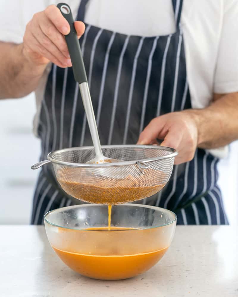 Straining the prawn stock through a sieve in a bowl