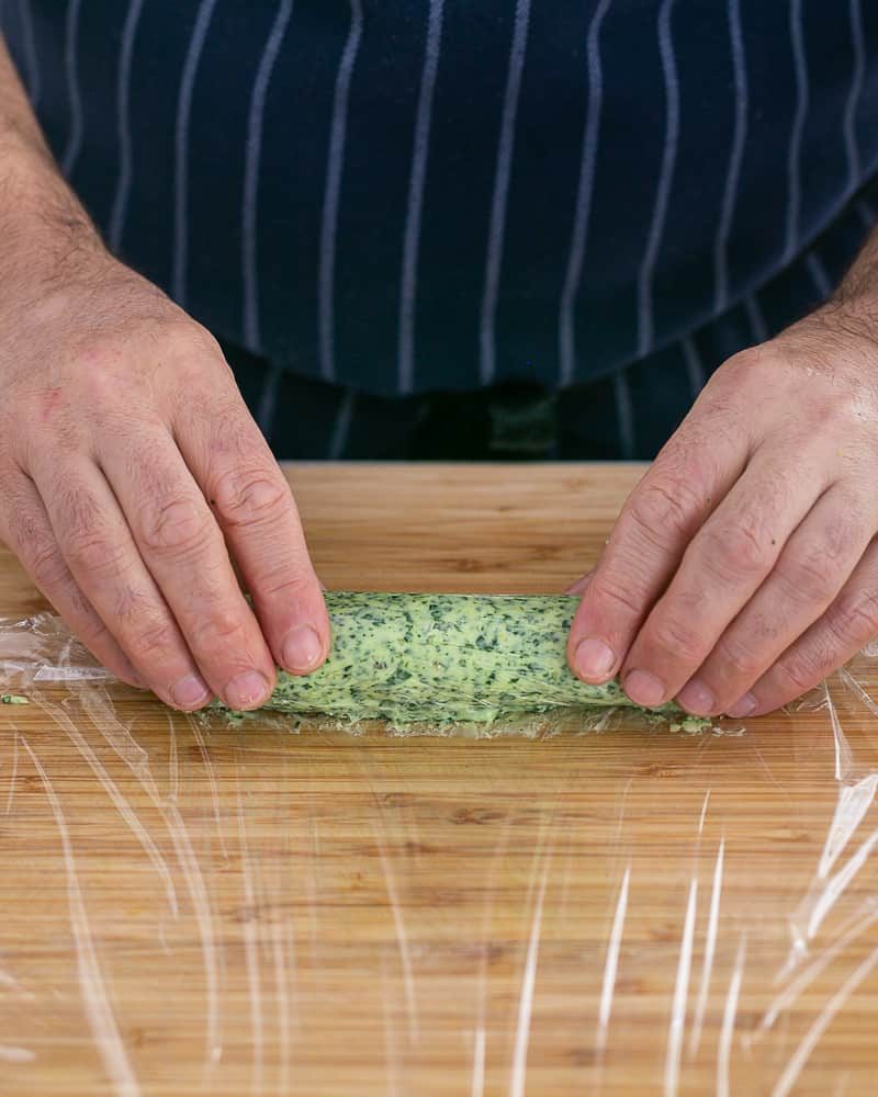 Person rolling the garlic herb butter in a cling wrap to form a log