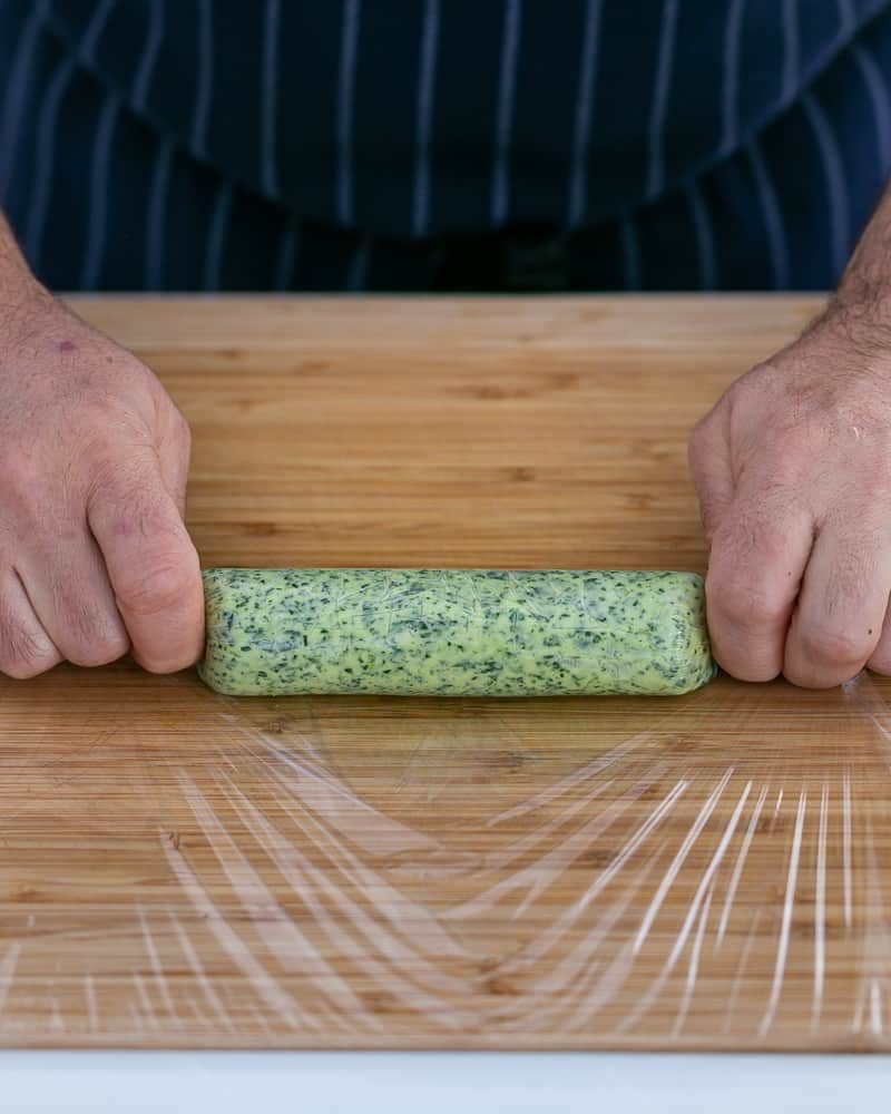 Person rolling the garlic herb butter in a cling wrap to form a log