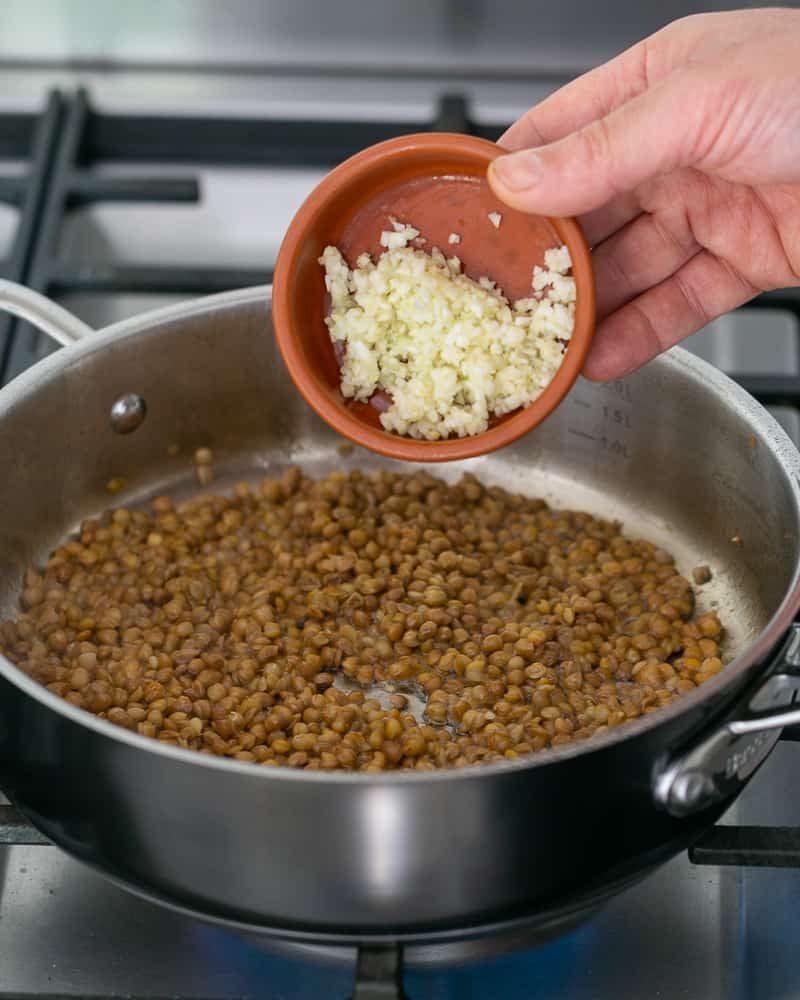 Chopped garlic added to brown lentils in pan to make Baked sweet Potato with Lentils and Swiss Chard