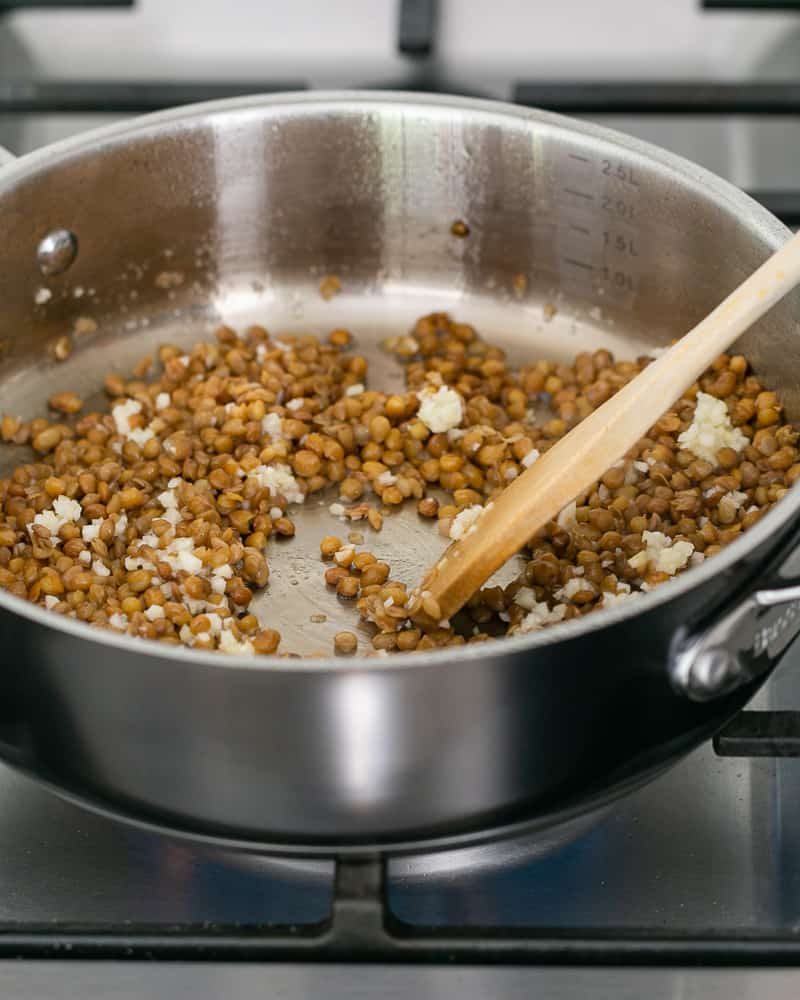 Chopped garlic added to brown lentils in pan to make Baked sweet Potato with Lentils and Swiss Chard