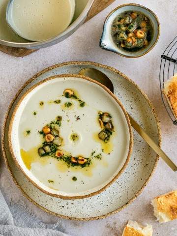 Jerusalem Artichoke Soup garnished with hazelnut butter and served in a ceramic bowl with bread on the side