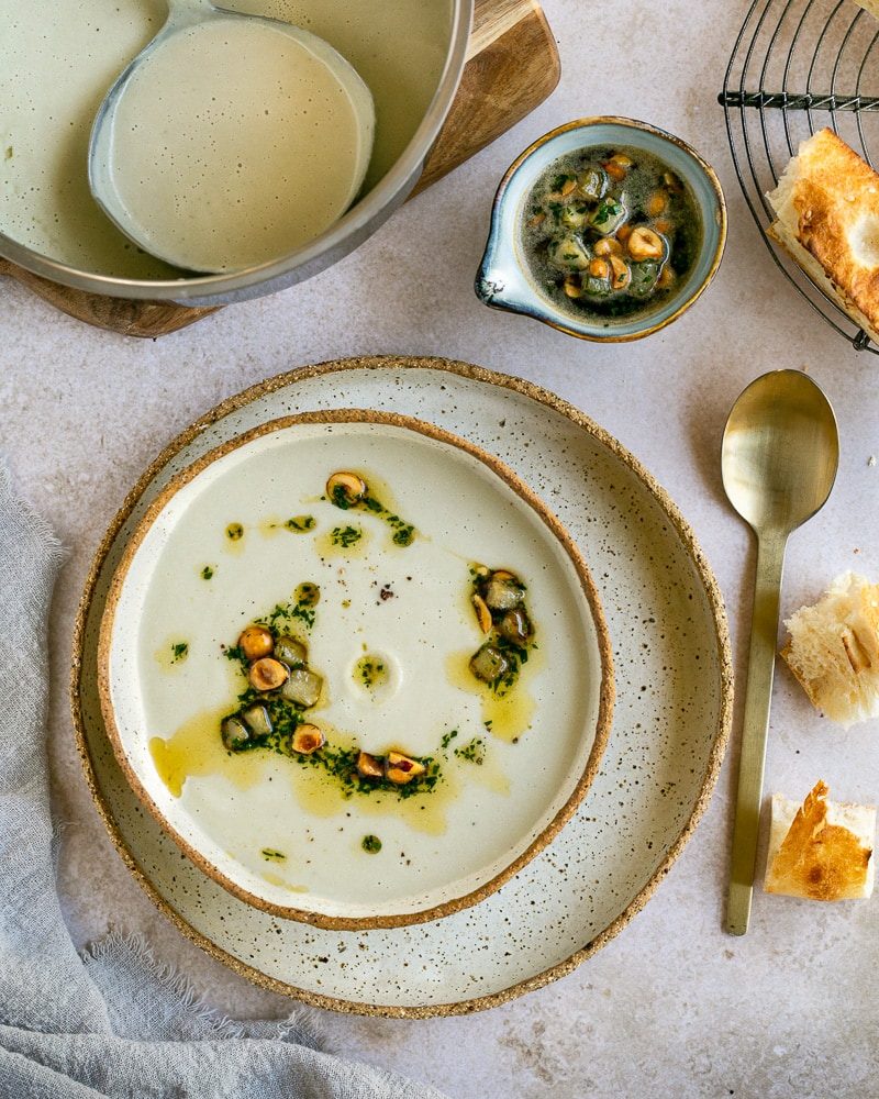 Jerusalem Artichoke Soup garnished with hazelnut butter and served in a ceramic bowl with bread on the side