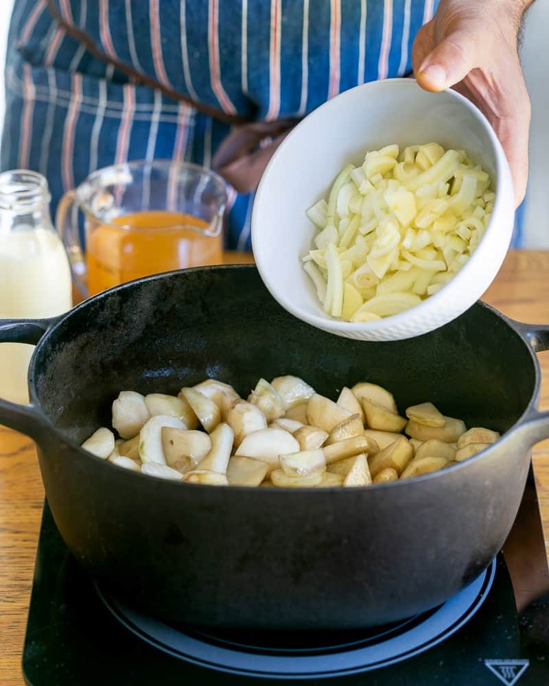 Sliced brown onions added to the sunchokes in the pot for jerusalem artichoke soup