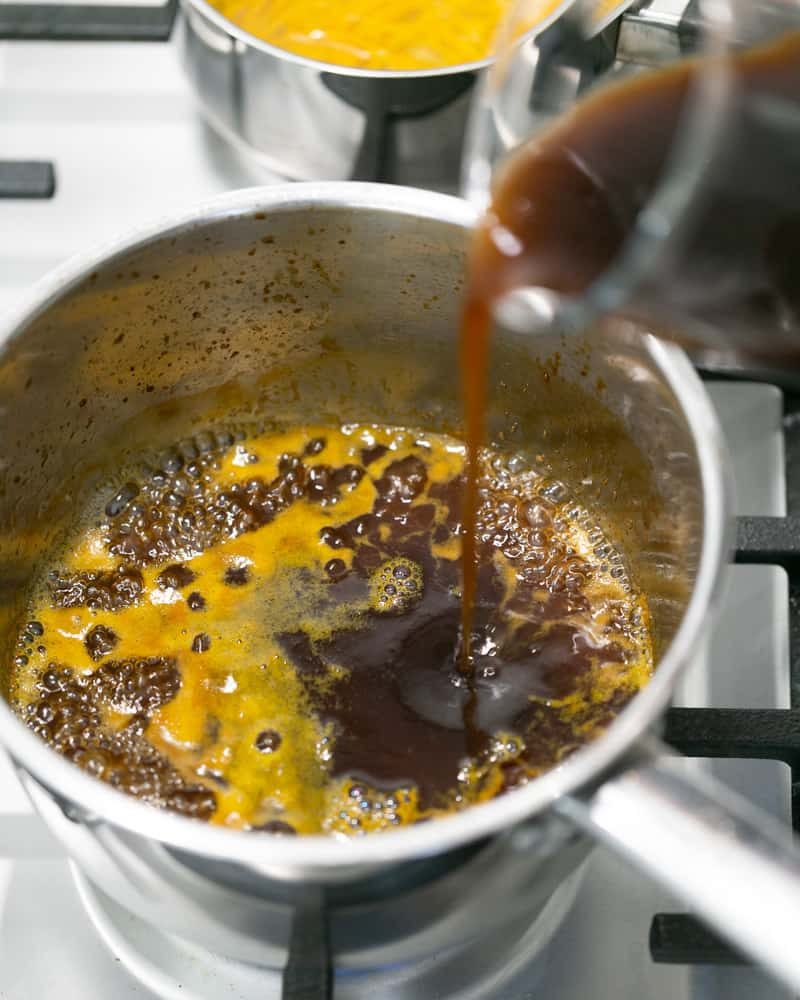 Chicken jus being added to caramel in pot over stove for sauce bigarade