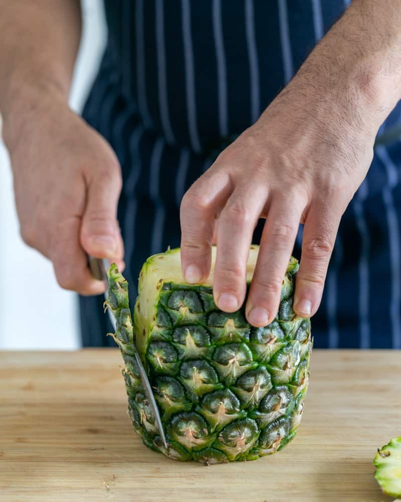 Whole pineapple being peeled with a sharp knife