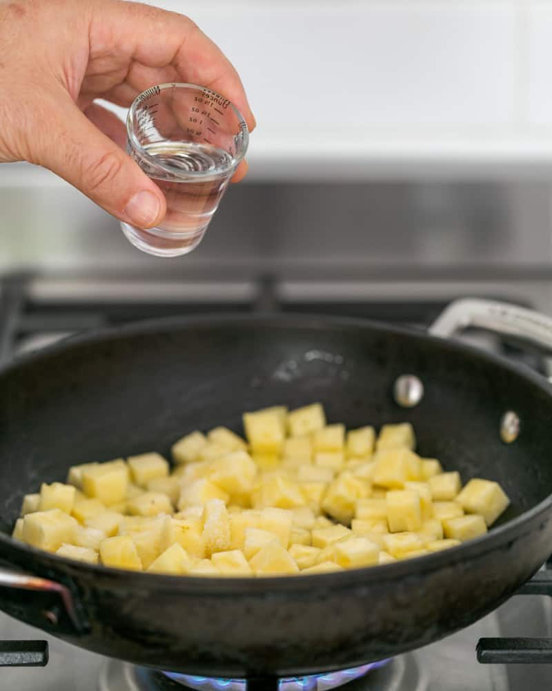 Diced pineapple in a pan with malibu rum in a shot glass for pouring