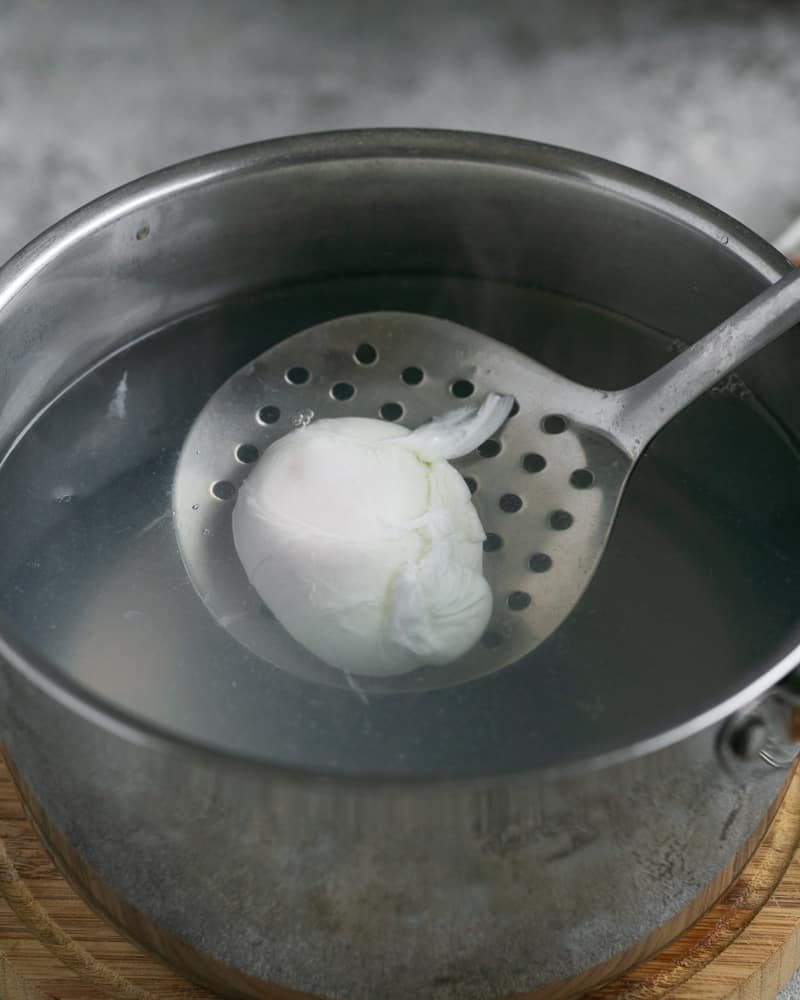 taking out a Poached egg with a slotted spoon from a pot of hot water