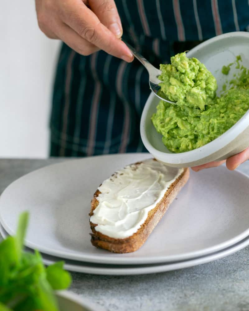 Taking a spoonfull of the crushed avocado from a bowl to spread on a slice of toasted sourdough