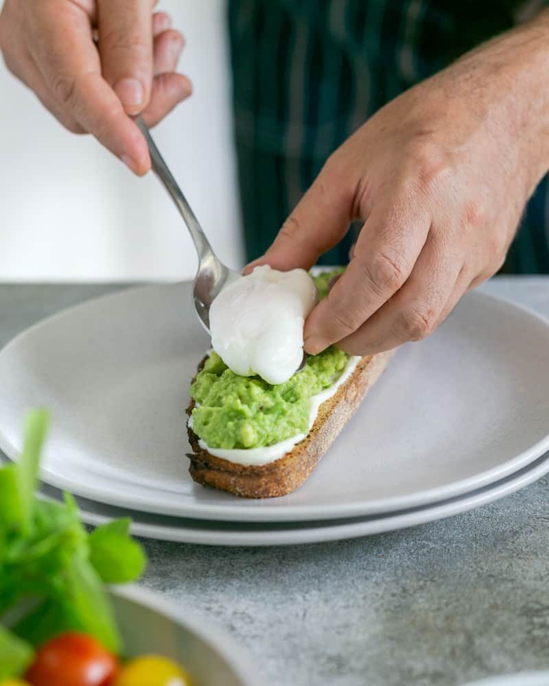 Placing a poached egg on top of avocado mix on toasted sourdough slice