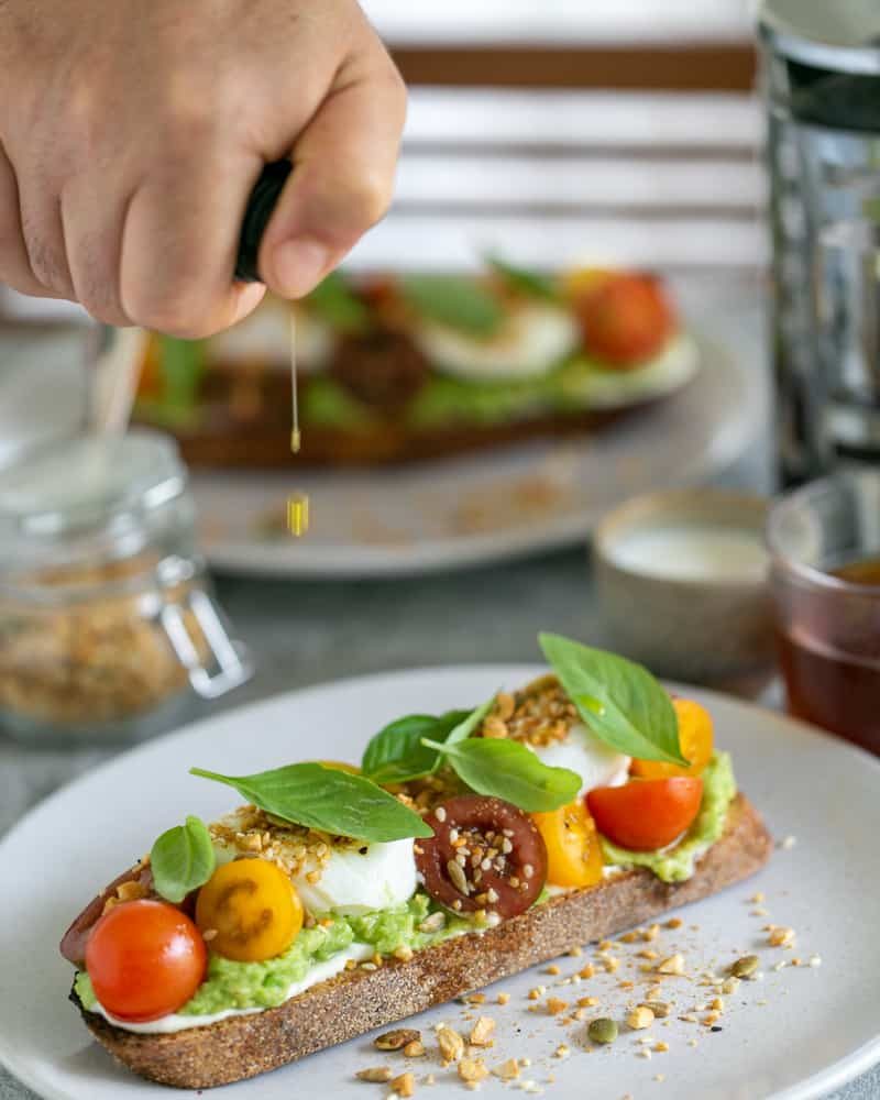 breakfast set up on table with Slice of sourdough with ricotta, crushed avocado, poached eggs, cherry tomatoes, basil and dukkah