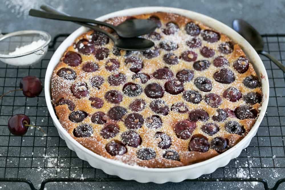 Freshly baked Cherry Clafoutis tart on a cooling rack with two black spoons