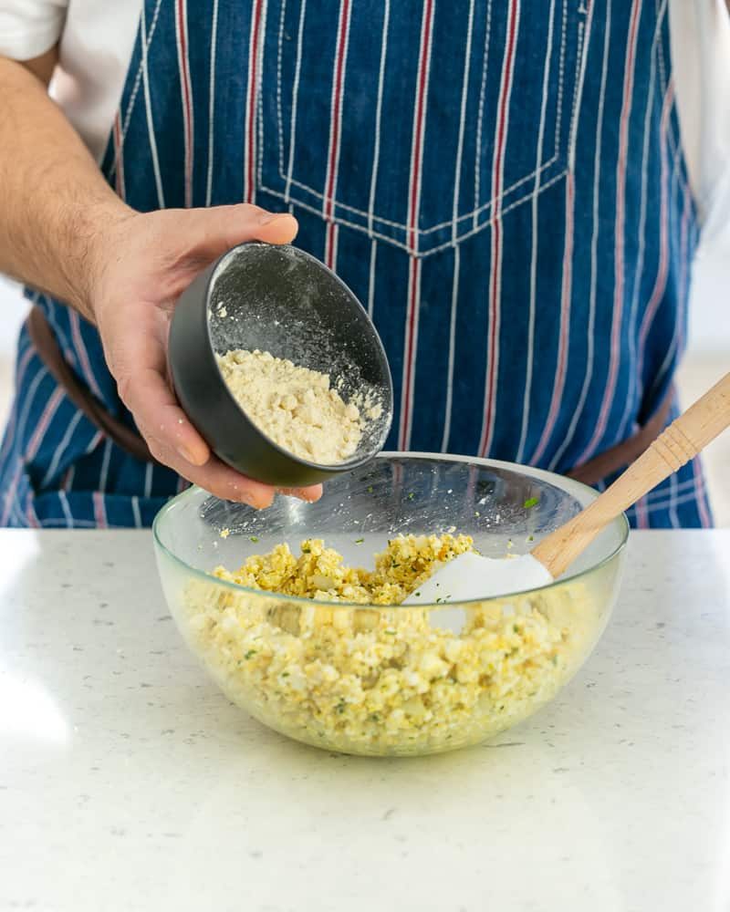 A person adding chickpea flour to paneer kofta mix