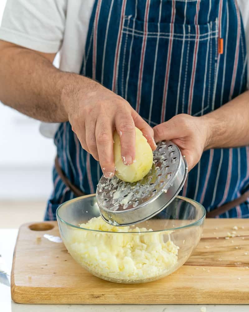 A person grating boiled potato in a bowl