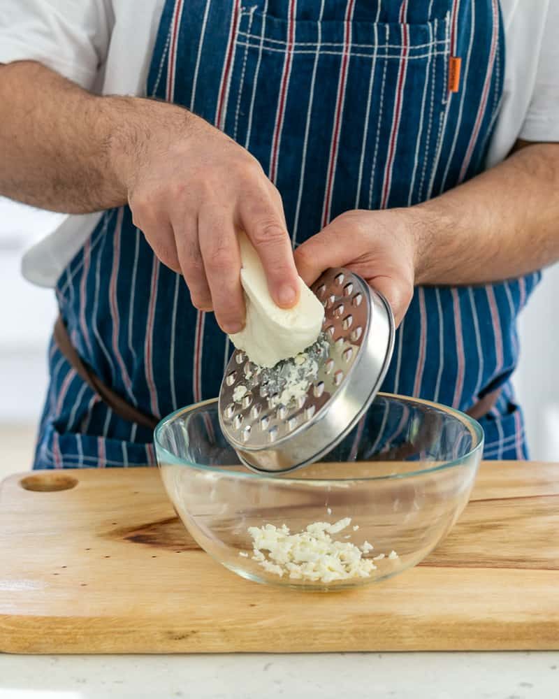 A person Grating fresh paneer in a bowl