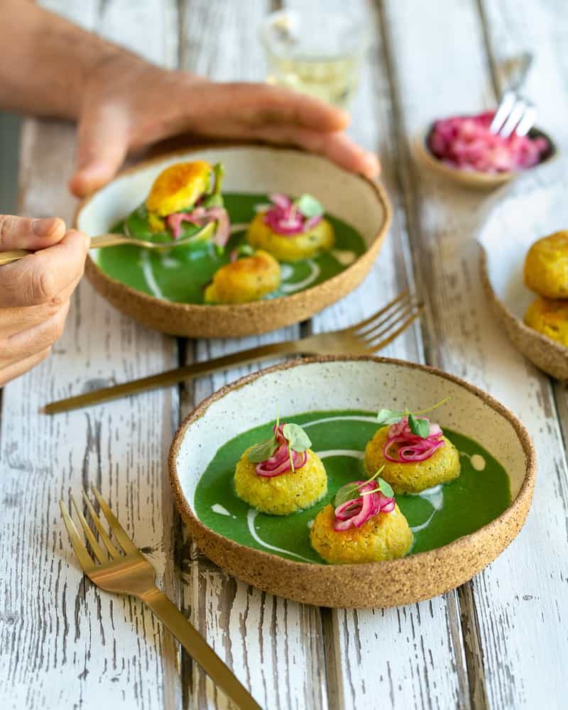 A person in the background eating Paneer and Potato Dumplings with Spinach Sauce