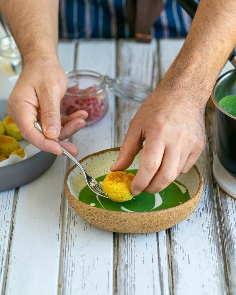 A fried paneer and potato dumpling placed in the middle of the bowl with the spinach soup