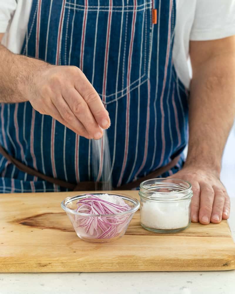 Adding salt to sliced onions to make pickled red onions for garnish