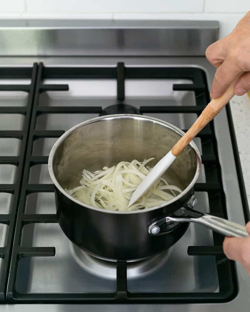 A person sautéing sliced onions and garlic in olive oil