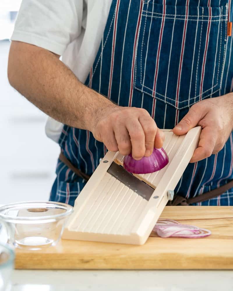 A person slicing red onions to be used as garnish on paneer and potato dumplings with spinach sauce