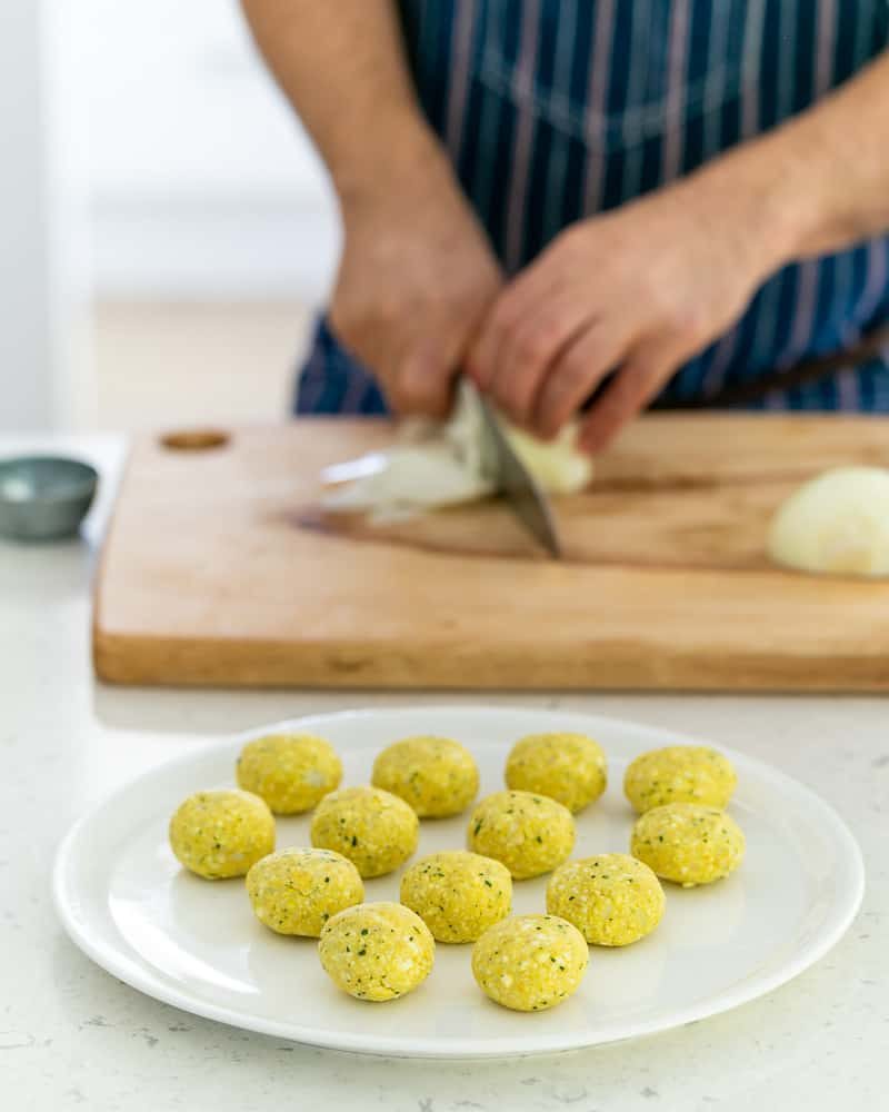 A person slicing onions with the the paneer and potato balls in the front