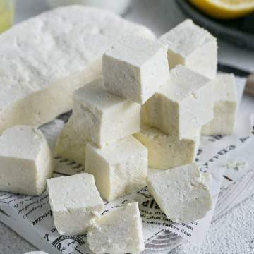 Paneer cut in cubes with half the paneer slab along with lemon juice and milk in background for How to make paneer