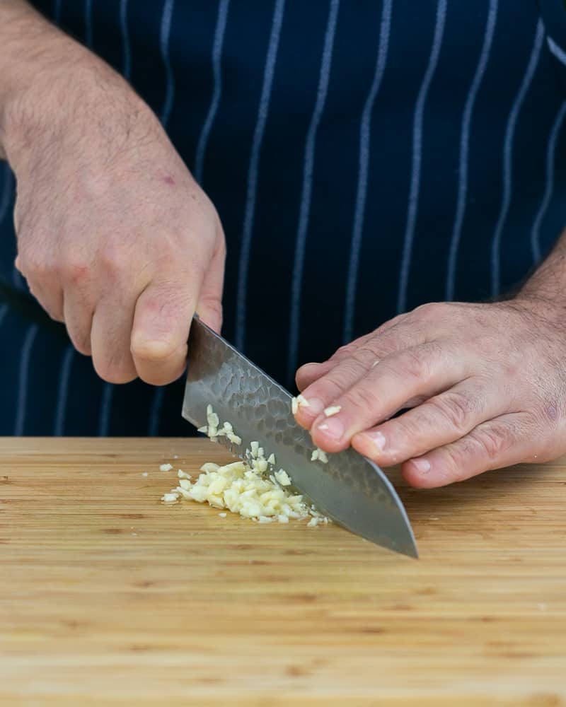 Person chopping crushed garlic with knife to make garlic Herb butter