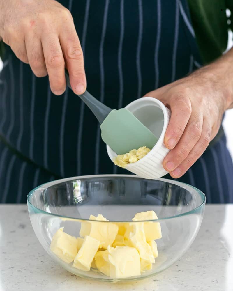 Person adding crushed garlic to butter to make garlic herb butter