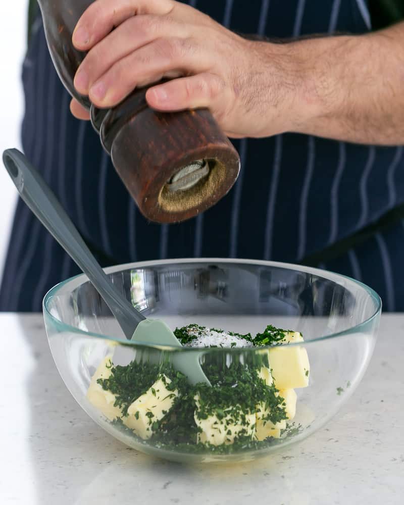 Person adding salt and pepper to butter to make garlic Herb butter