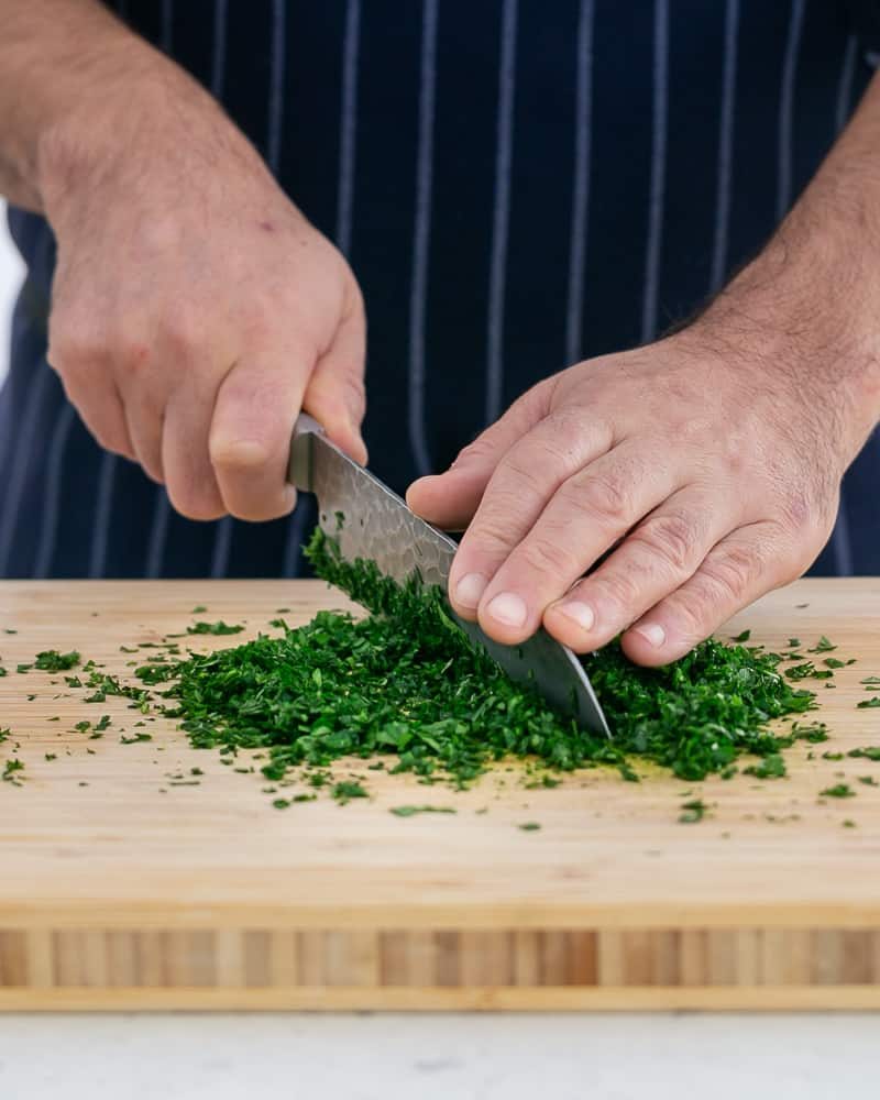 Person chopping parsley with a knife to make garlic Herb butter