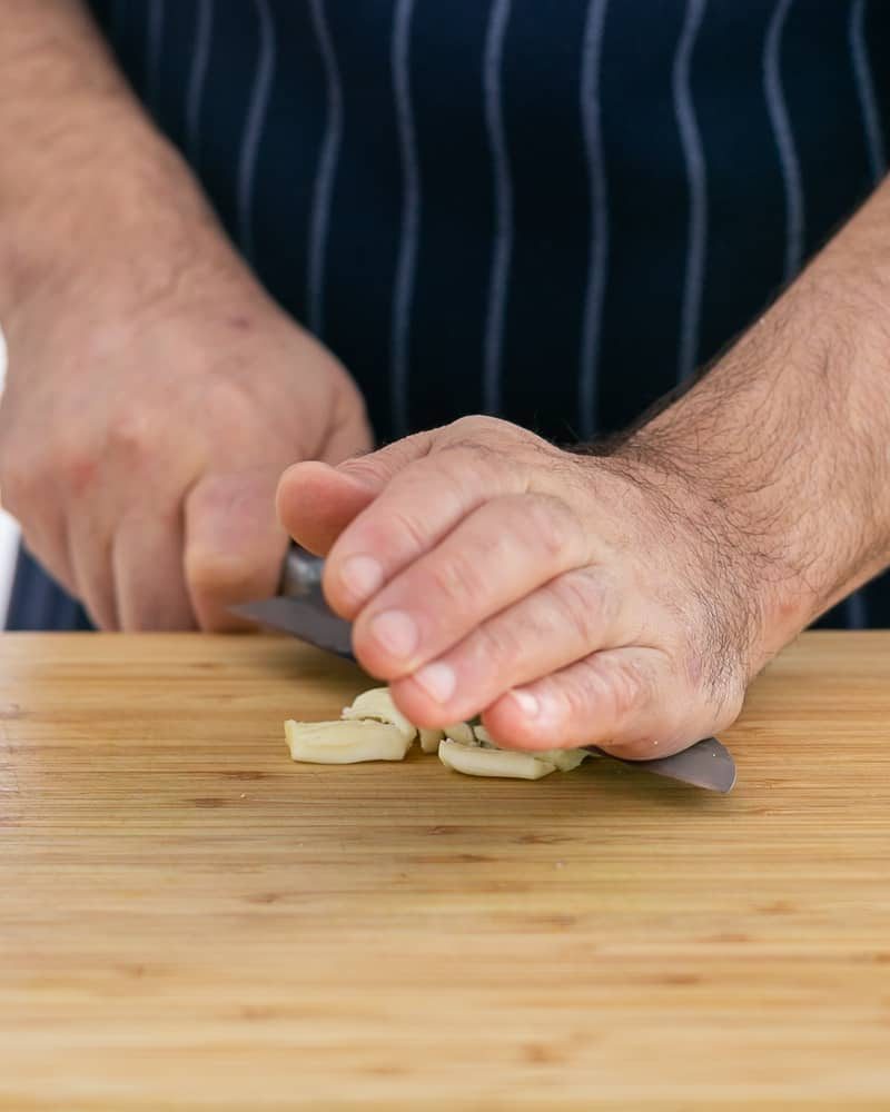 Person crushing peeled garlic with knife to make Garlic Herb butter