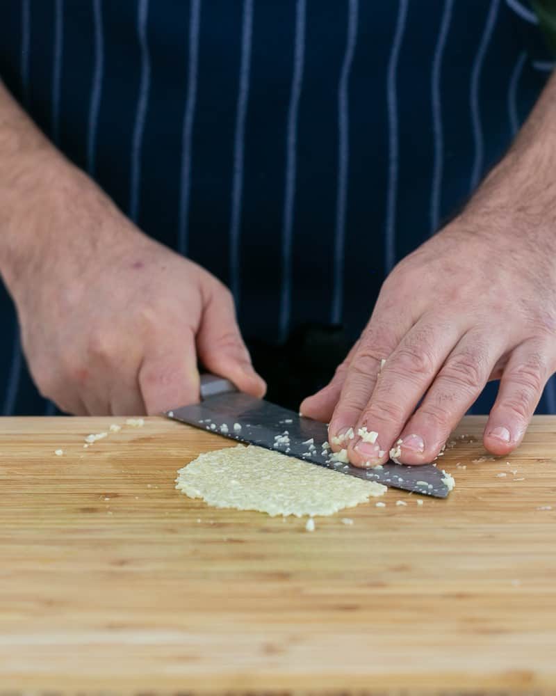 Person crushing chopped garlic with knife to make garlic herb butter