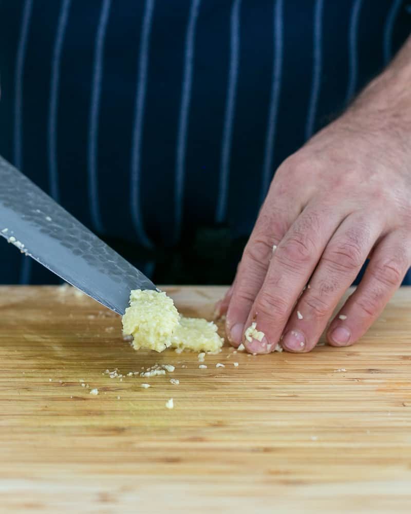 Person showing garlic paste on knife to make garlic Herb butter