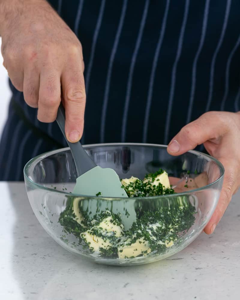 Person mixing all ingredients in a bowl to make garlic herb butter