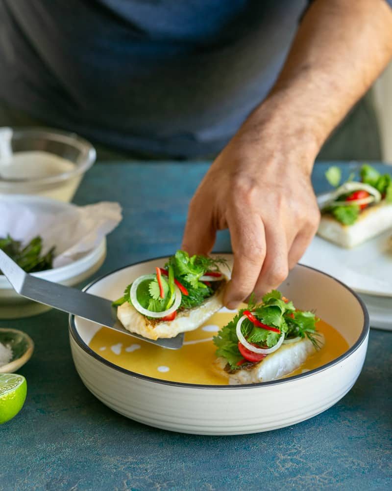 using a spatula turned fish fillets placed on the coconut curry sauce in bowl