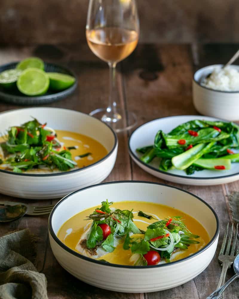 Seared red snapper with coconut curry sauce served in deep white bowls with rice and green vegetables on the side