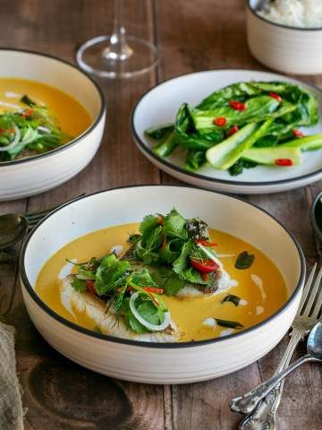 Red snapper with coconut curry sauce served in a deep white bowl garnished fresh herbs