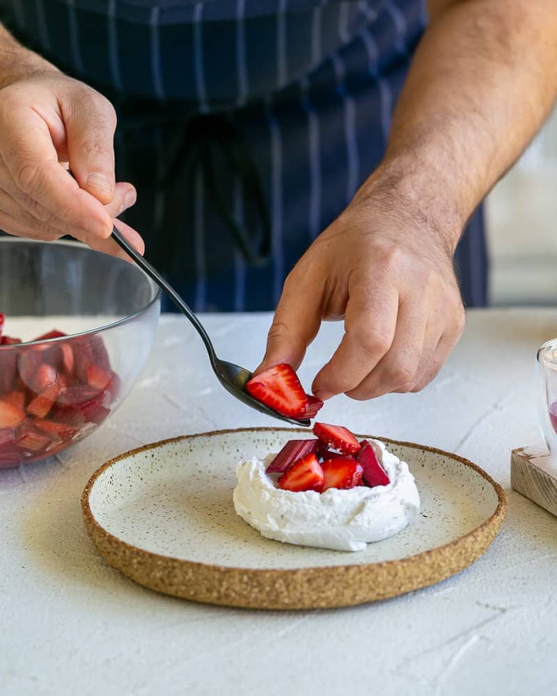 Placing spoonful strawberries and rhubarb on the whipped cream in the plate