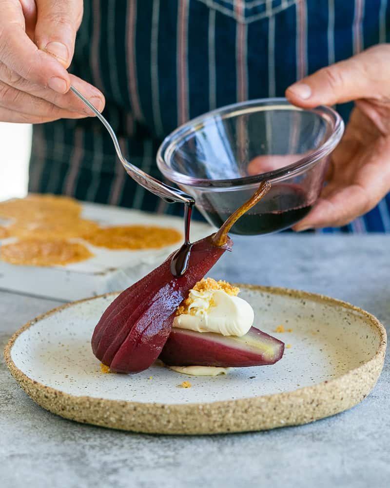 Pouring the wine syrup over the poached pears with the mascarpone and nut brittle