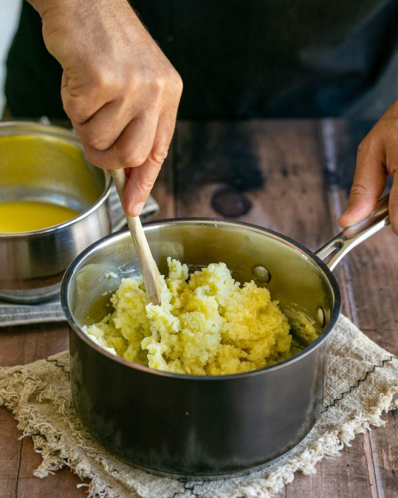 Mixing mashed potatoes with milk and butter mix using a wooden spoon