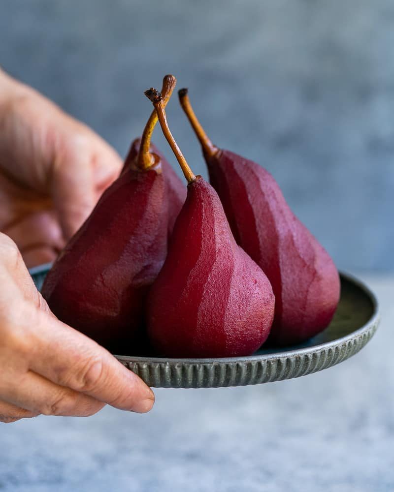 Four poached pears in red wine on a metal plate