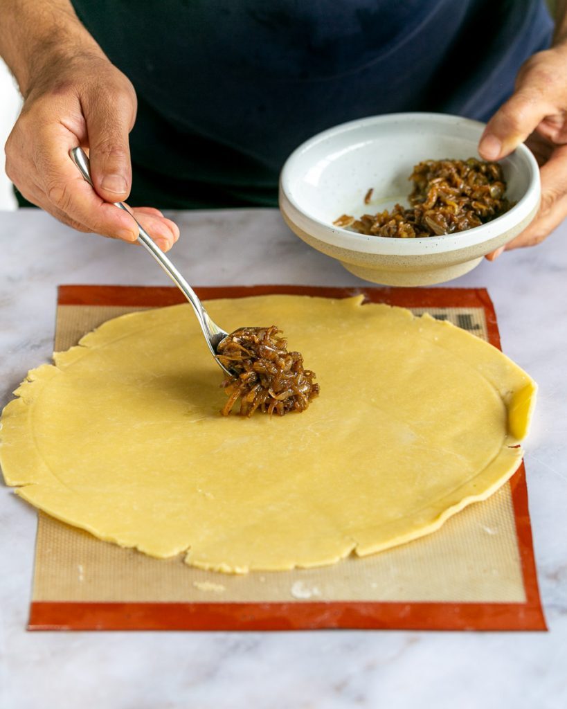 spreading caramelized onions on the round pastry