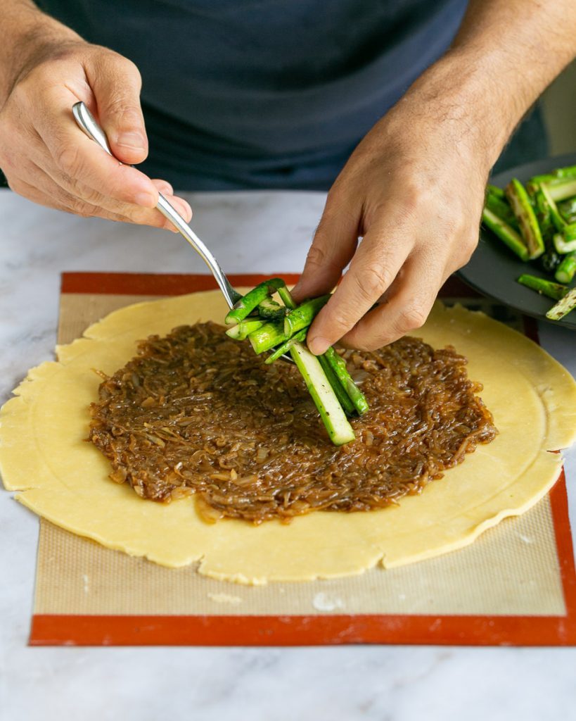 Adding the roasted asparagus on teh caramelized onion spread