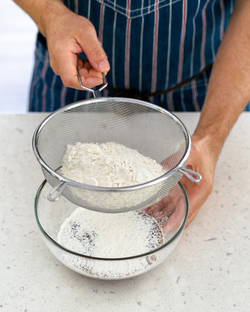 Sifting flour into the prepared caramel in the bowl