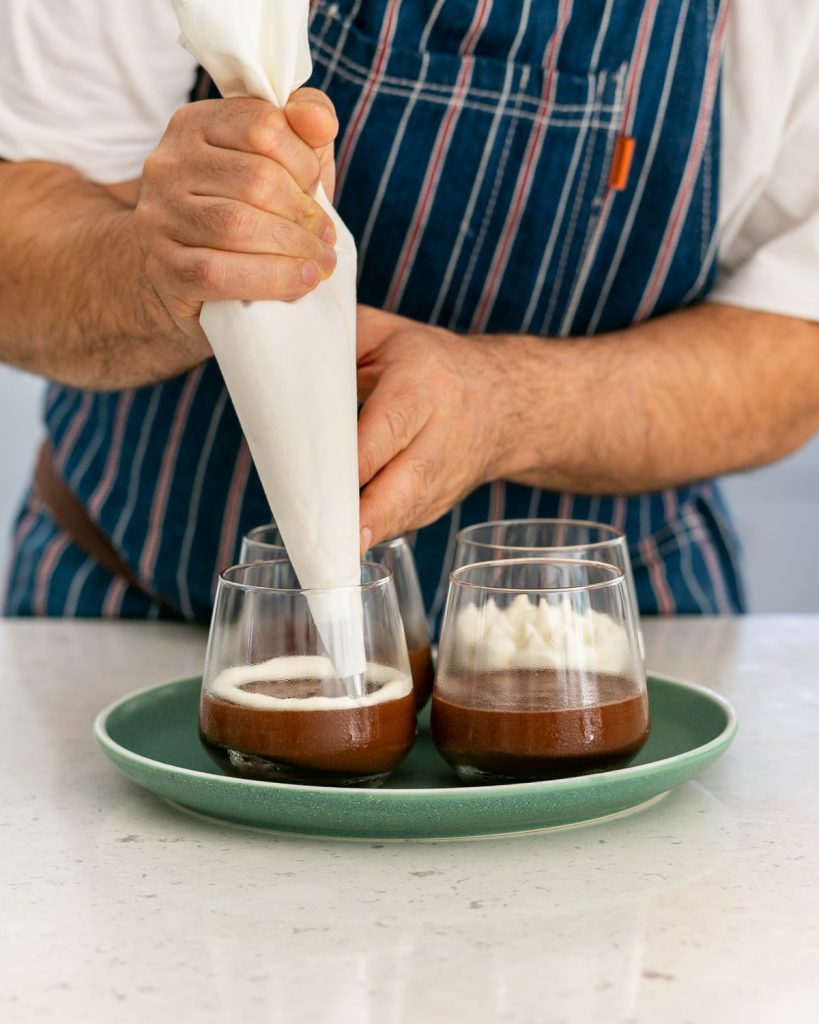 Piping whipped cream over chocolate mousse in glass