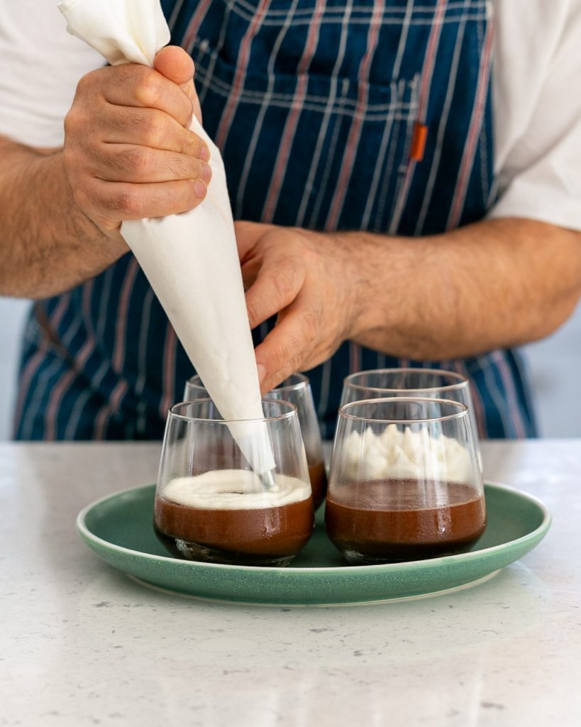 piping whipped cream in circles over chocolate mousse