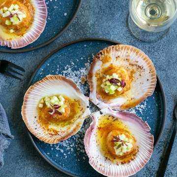 Three Oven Baked Scallops with Miso and Ginger Butter in a plate with a glass of wine on the side